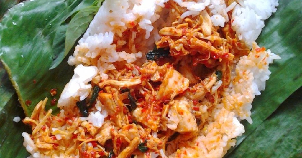 Sajian nasi bakar ayam suwir kemangi yang dibungkus daun pisang di atas piring.